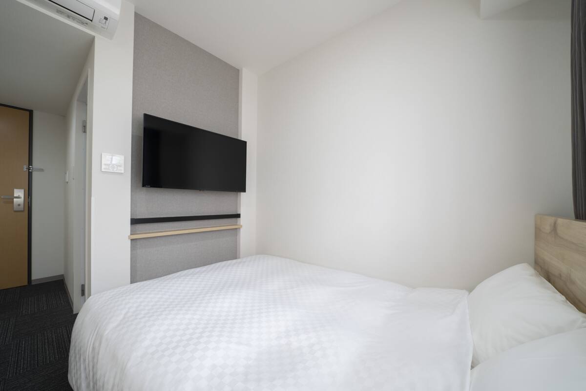 Ett hotellrum med en säng, en TV som hänger på väggen och en dörr.