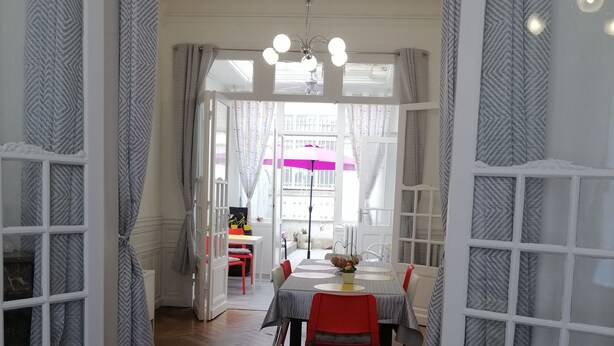 Un comedor con suelo de madera en diseño espiga, una mesa con mantel blanco, sillas rojas y un ventilador de techo.