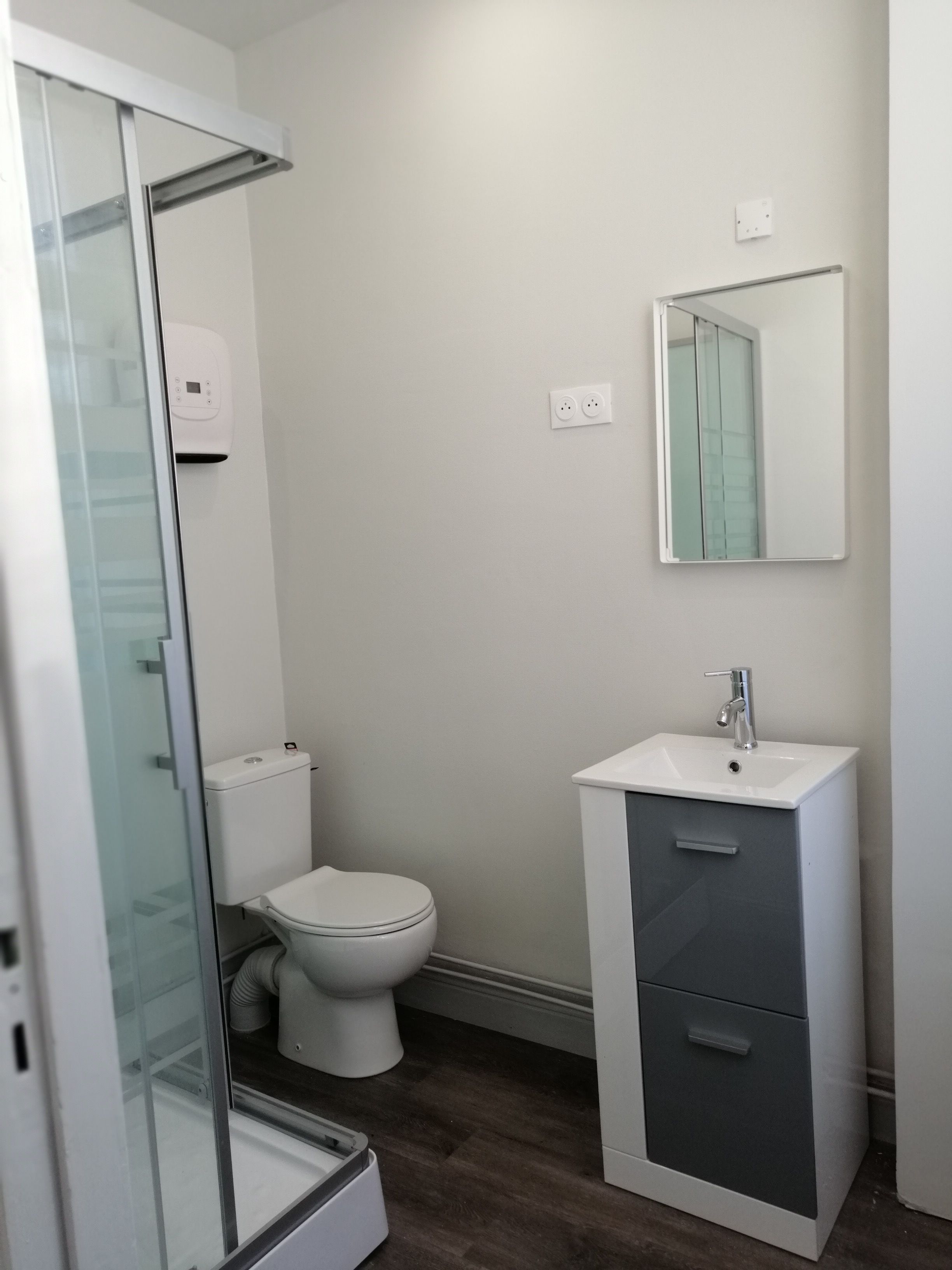 Une salle de bain avec une douche à parois de verre, des toilettes, un lavabo avec un miroir et un meuble de rangement.