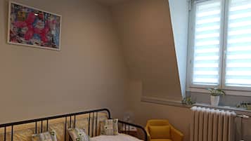 Een slaapkamer met een bed, een gele stoel, een radiator en een raam met zonwering.