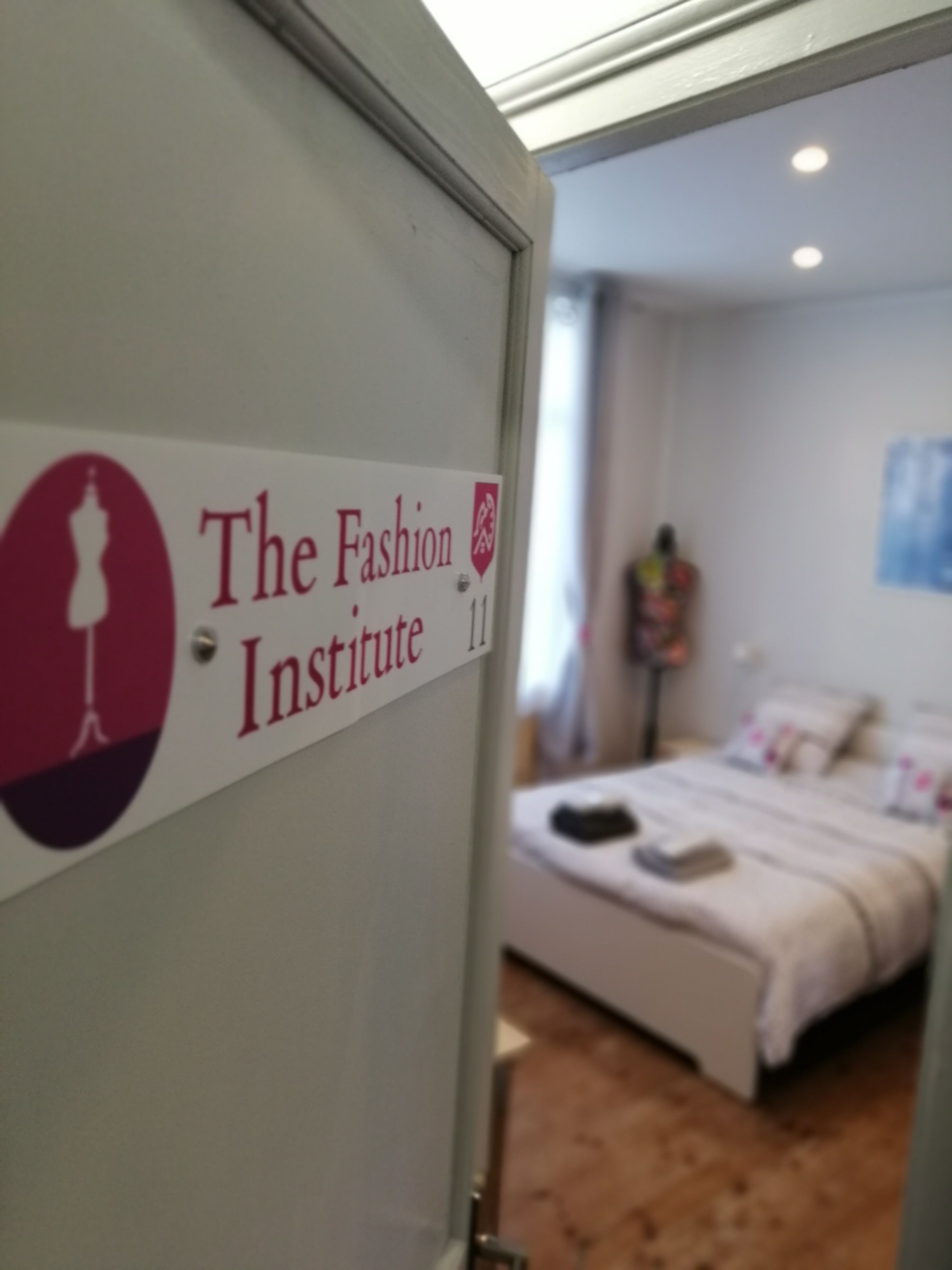 A sign for The Fashion Institute with a bed and a nightstand in the background.