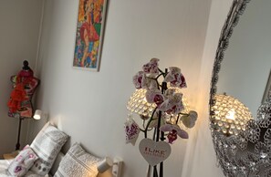 Una habitación con una orquídea ornamental, un maniquí, almohadas estampadas y un cuadro en la pared.