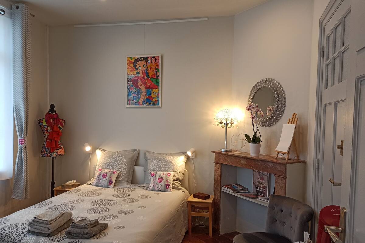 Un dormitorio ordenado con cama, mesitas de noche, cómoda, silla y un espejo montado en la pared.