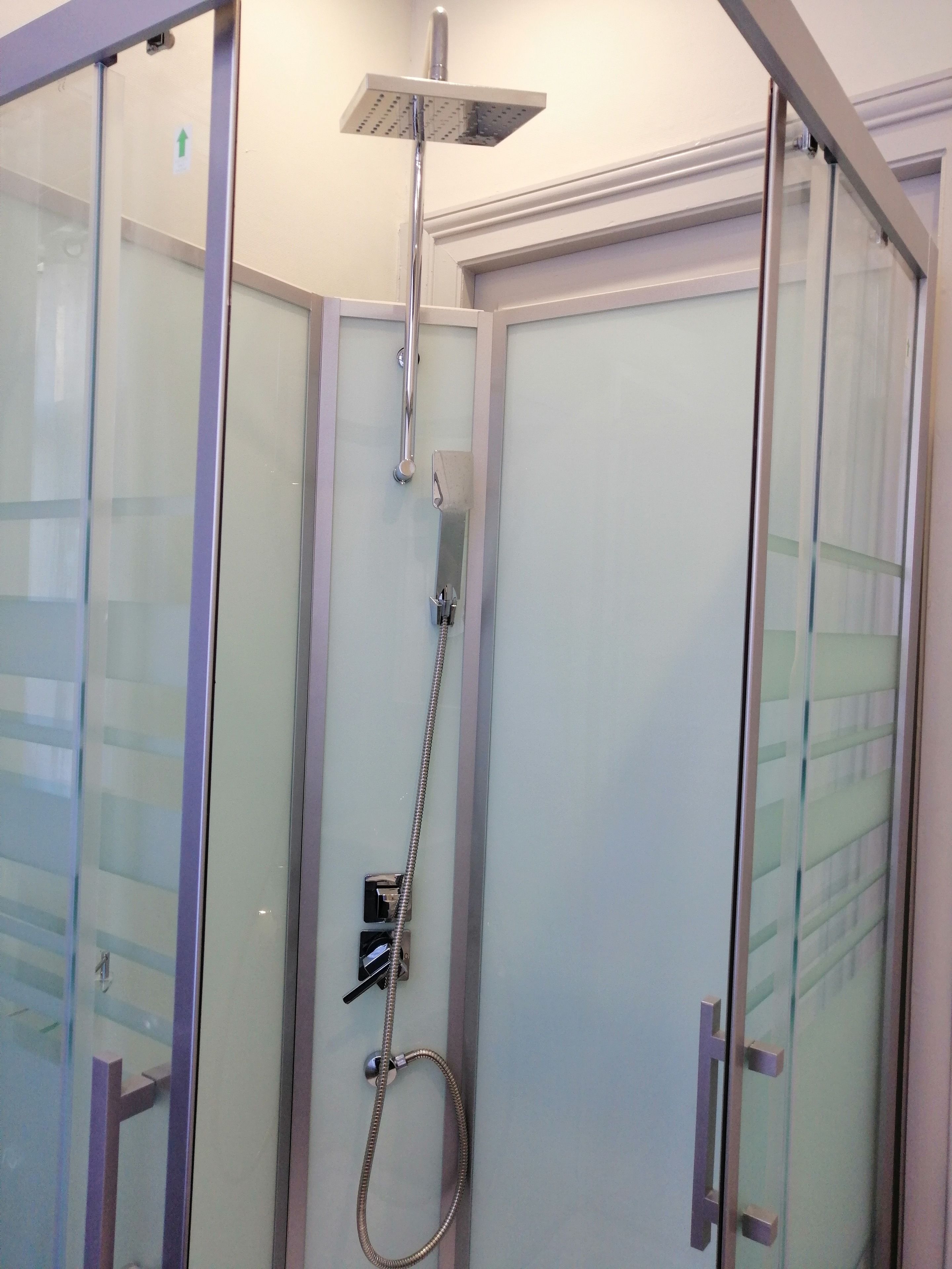 A glass-enclosed shower stall with a handheld showerhead and a fixed overhead showerhead.