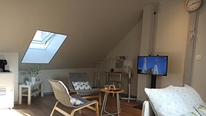 Una habitación moderna y luminosa con techo inclinado, tragaluz, televisor, escritorio, silla y cama.