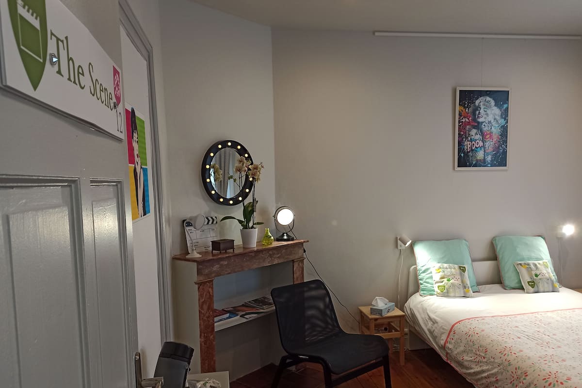 Un dormitorio con cama, escritorio con espejo, silla, mesita de noche y un póster en la pared.