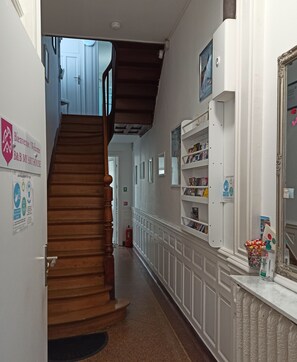 Un pasillo con una escalera de madera, paredes blancas y un estante con varios objetos.