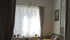 Una habitación con cama, una mesa con sillas, un ventanal con cortinas y una lámpara en el techo.