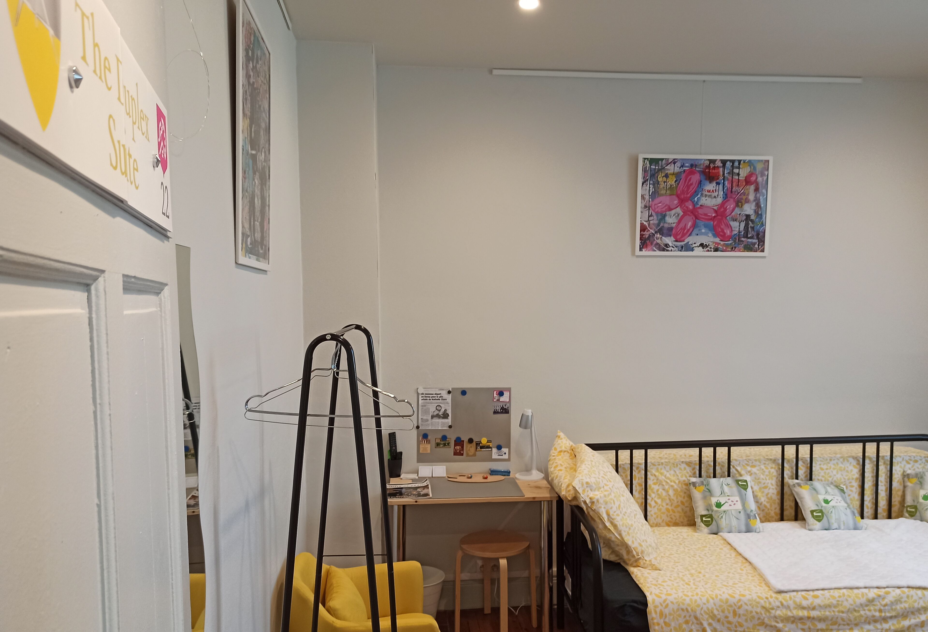 A bedroom with a bed, desk, chair, and a wall-mounted shelf.