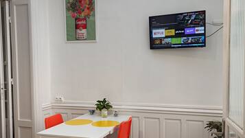 A dining area with a white table, red chairs, and a TV mounted on the wall displaying various streaming services.
