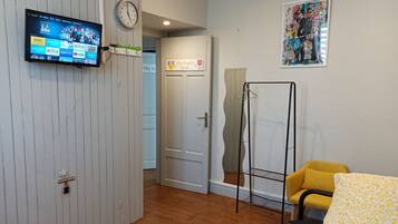 Una habitación de hotel con un televisor montado que muestra servicios de transmisión, una puerta con la etiqueta "The Duplex Suite 22", una silla amarilla y un estante fijado a la pared.