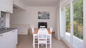 A modern kitchen with white cabinets, a dining table with chairs, a flat-screen TV, and a balcony with a view of trees. - S160 - Sirolo, brand new two-room apartment with terrace (Sirolo)