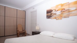 A bedroom with a bed, a chair, a nightstand, a lamp, and a wall with a painting. - S160 - Sirolo, brand new two-room apartment with terrace (Sirolo)