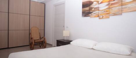 A bedroom with a bed, a chair, a nightstand, a lamp, and a wall with a painting.