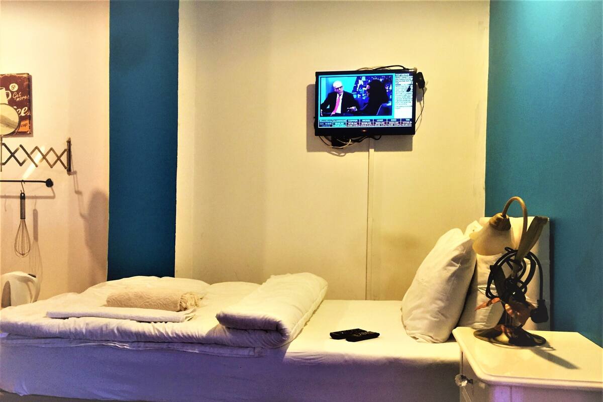 A hotel room with a bed, a TV mounted on the wall, and a bedside table with a lamp.