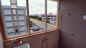 Casa de banho com janela e vista para a paisagem urbana, incluindo uma estrada e edifícios.