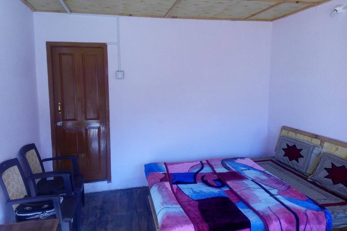Ein Schlafzimmer mit Holztür, einem Bett mit gemusterten Betttextilien und einem Sessel.