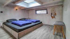 A bedroom with a skylight, a bed with blue bedding, a small table, a dreamcatcher, and a wooden bench.