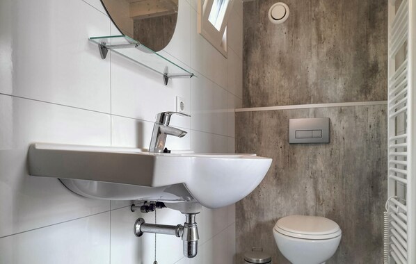 Un baño moderno con lavamanos, espejo y retrete blancos.