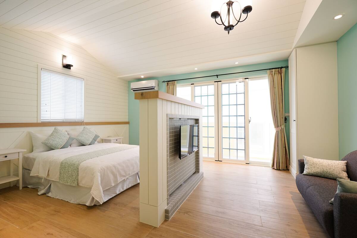 A spacious bedroom with a large bed, a TV mounted on a wall, and a sliding glass door leading to a balcony.