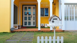 A yellow house with a white porch, a welcome sign, a 'Good Time' sign, and a small white mailbox. - Good Time (Magong)