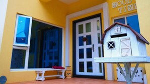 A yellow building with a white door and a small white structure resembling a shed. - Good Time (Magong)