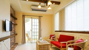 A room with a brick wall, a flat-screen TV, wicker chairs with red cushions, a wooden table, and a sliding glass door leading to an outdoor area. - Good Time (Magong)