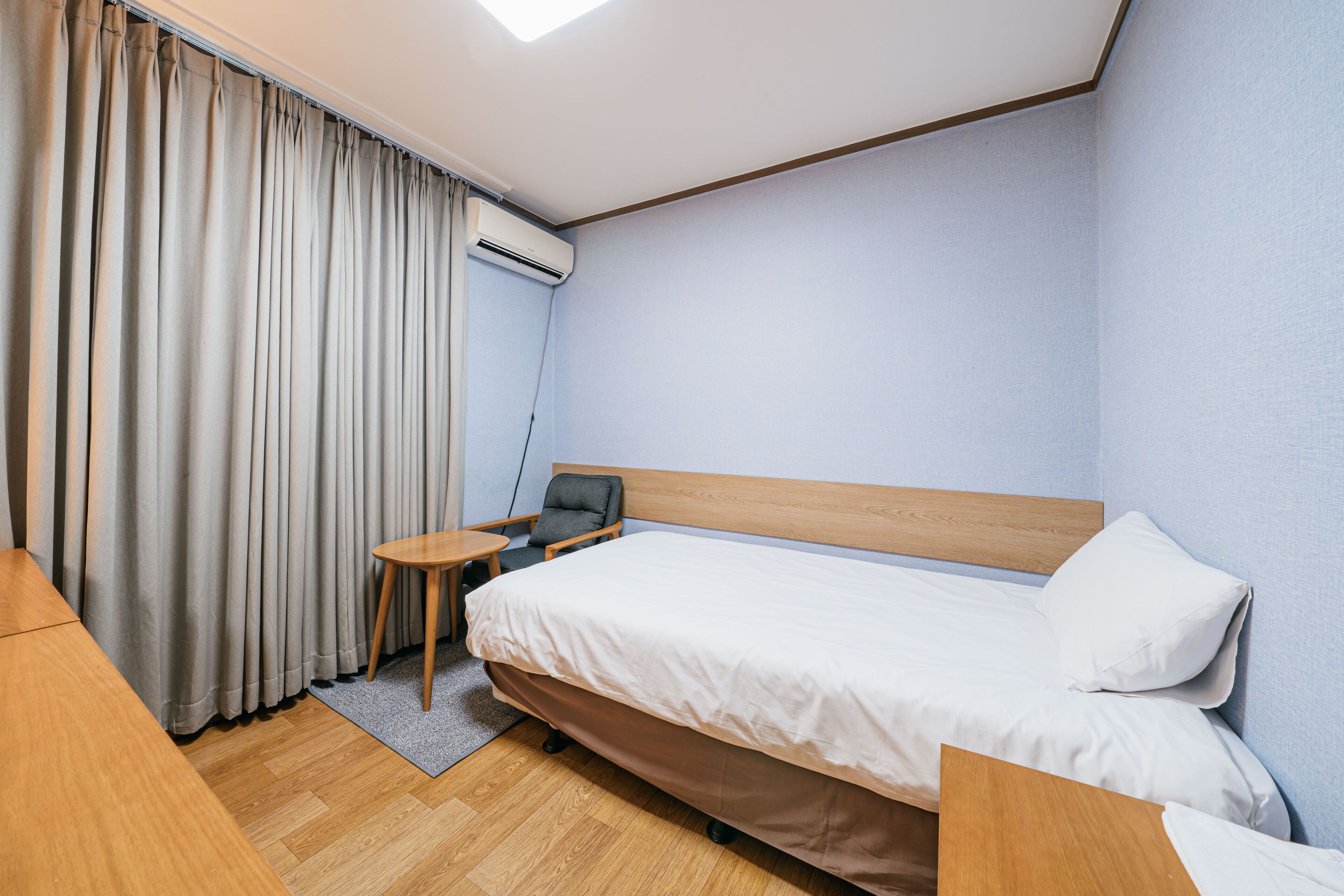 Ein Hotelzimmer mit einem Einzelbett, einem kleinen Tisch, einem Stuhl und einer Klimaanlage.