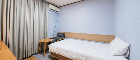 Ein Hotelzimmer mit einem Einzelbett, einem kleinen Tisch, einem Stuhl und einer Klimaanlage.