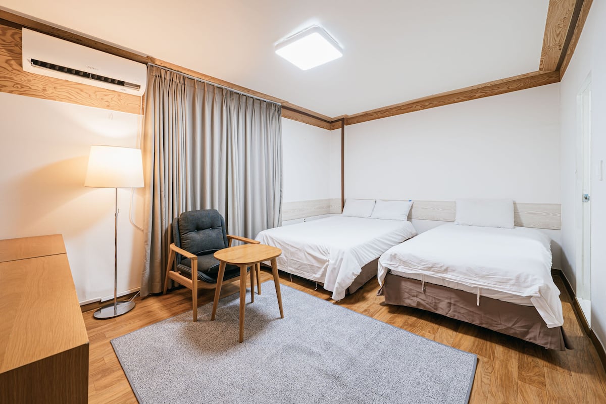 Une chambre d’hôtel avec deux lits, un bureau, une chaise, une lampe et une fenêtre avec des rideaux.