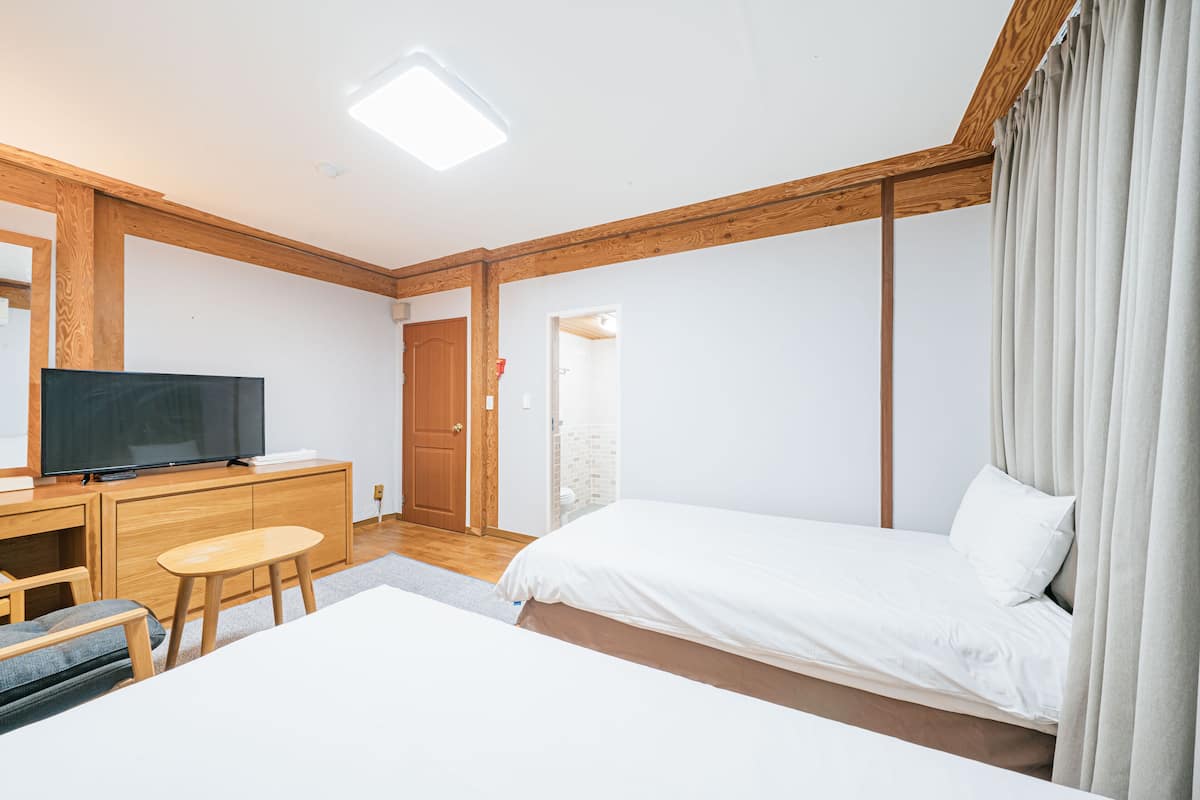 Une chambre d’hôtel moderne, équipée d’un lit, d’un téléviseur posé sur une commode en bois, d’une petite table et d’une porte donnant sur une autre pièce.
