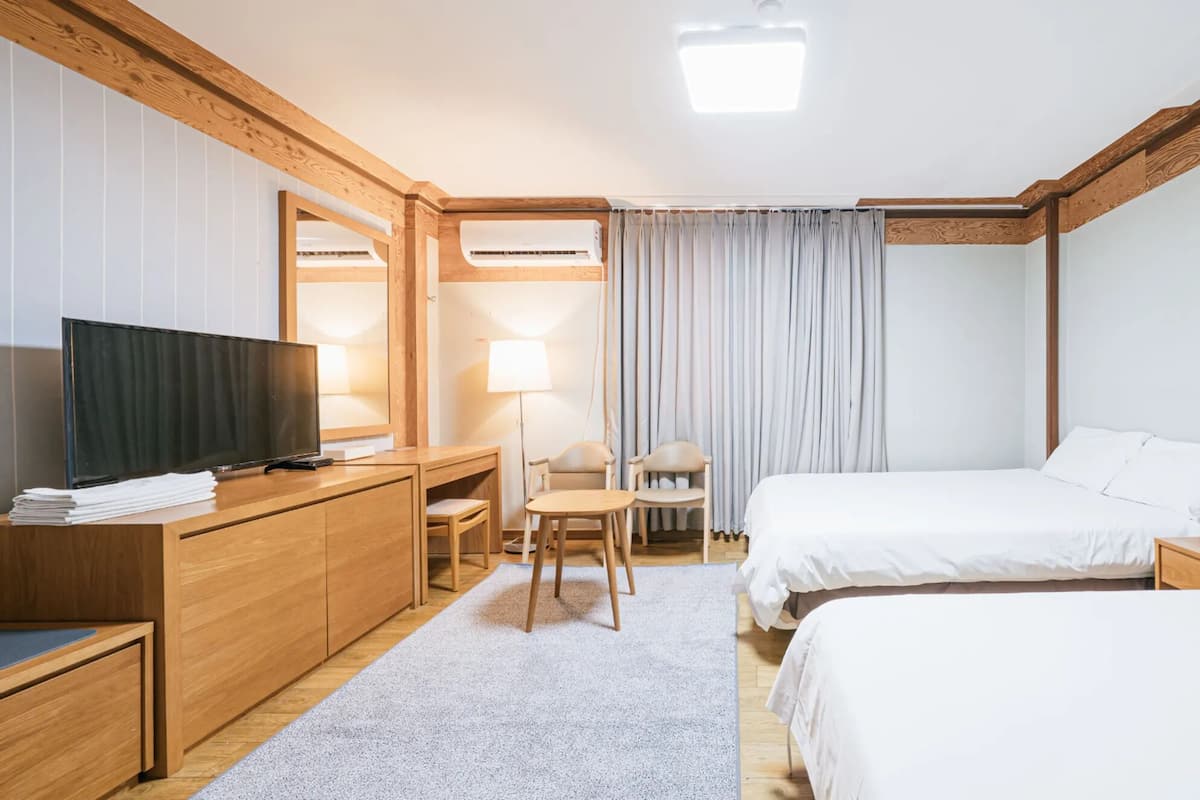 Une chambre d’hôtel avec un bureau en bois, une télévision, deux lits, une chaise et une lampe.