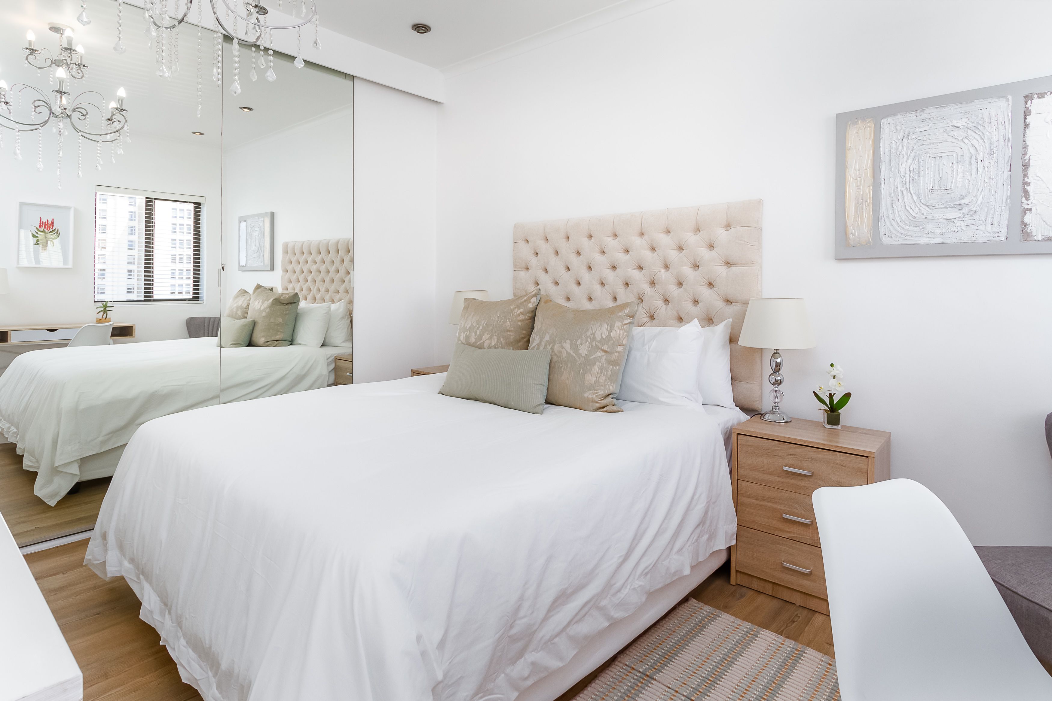 A modern bedroom with a large bed, a bedside table, a mirror, and a wall-mounted artwork.
