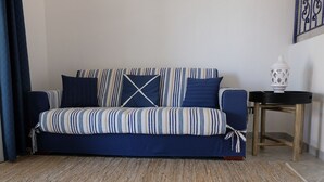 A dark blue sofa with striped cushions and a matching throw blanket, a woven rug, and a white lantern on a wooden side table. - Villa Cinzia sea view (Porto Tramatzu)