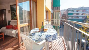 A balcony with a table set for two, a bed with red pillows, and a view of the cityscape. - 2 bedroom beautiful apartment in Pineda de Mar (Pineda de Mar)