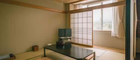A traditional Japanese room with tatami flooring, a low table, cushions, a television, and a sliding shoji screen.