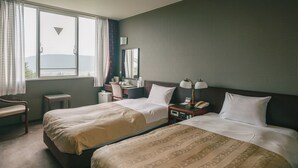 Habitación de hotel con dos camas, un escritorio, una silla, una mesita de noche con lámpara y una ventana con cortinas.