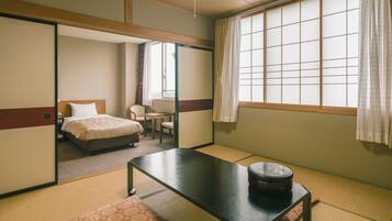 A traditional Japanese-style room with tatami flooring, a bed with a white pillow, a small table with a black container, and a sliding door leading to another room.