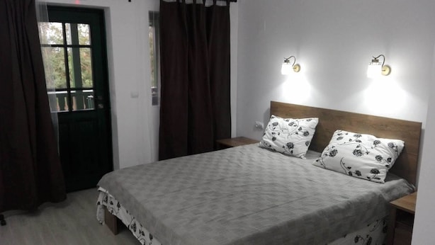 Un dormitori amb un llit, dues taules de nit, un panell de capçalera de fusta, una finestra amb cortines i llums penjades a la paret.