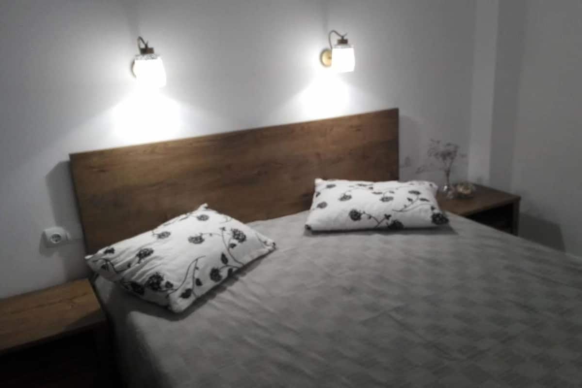 A bedroom with a wooden headboard, two bedside tables, and two wall-mounted lights.