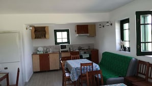 Cuina compacta amb microones, rentapesos i fogó. Hi ha dues taules de menjador amb cadires, un sofà verd i una finestra petita amb vistes.