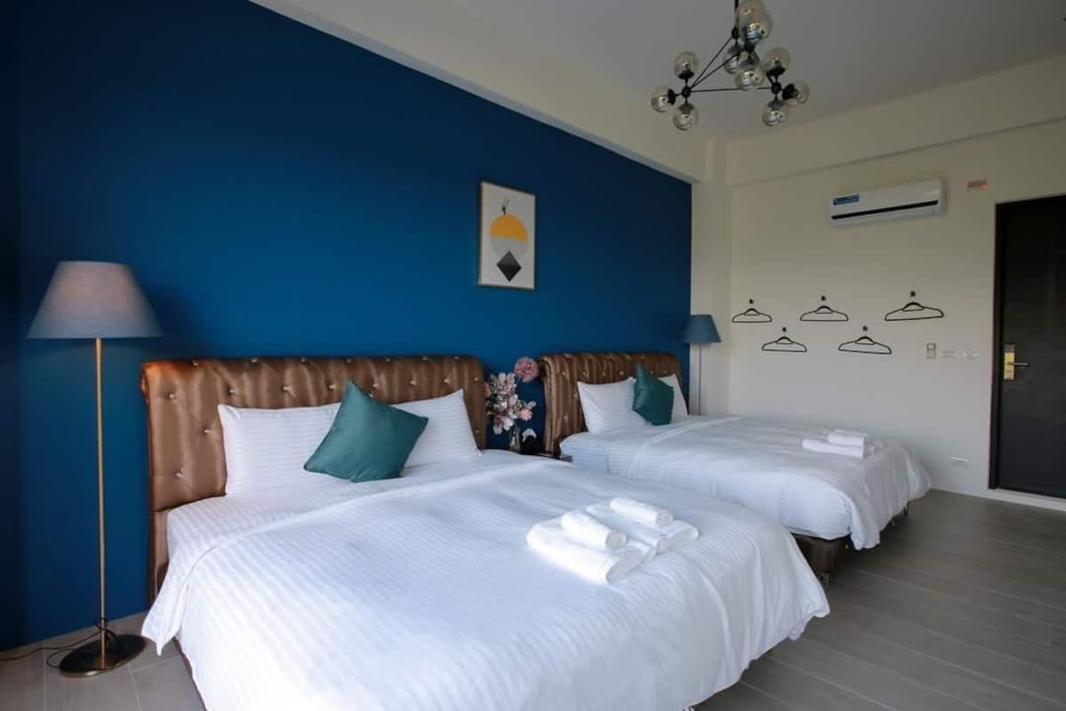 Habitació d'hotel amb dos llits, una paret blava, un lampadari i un aparell d'aire condicionat.