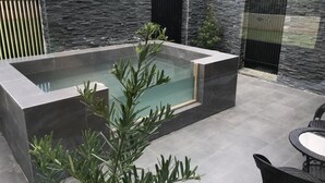 A modern outdoor pool area with a rectangular pool, surrounded by stone walls and a tiled patio. - Easy Inn (Hengchun)