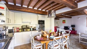 Una cocina con armarios blancos, una mesa de comedor de madera y sillas. Hay una araña colgando del techo.