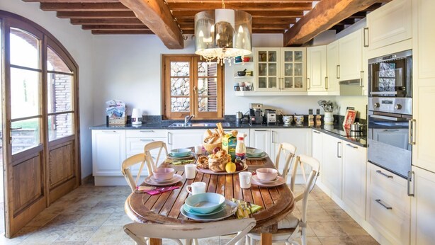 Una cocina con armarios blancos, una mesa de madera dispuesta para comer y un ventanal grande.
