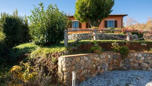 Un muro de piedra con una cerca de madera, un árbol y un edificio con tejado de tejas.