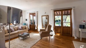 Un salón amplio con suelo de madera, un sofá color beige, una mesa de centro y un ventanal con cortinas.