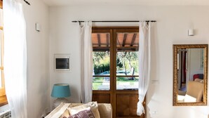 Una habitación con suelo de madera, un sofá color beige con cojines estampados, una lámpara azul, una puerta de madera con paneles de vidrio y un espejo grande con marco dorado.