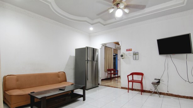 Una sala de estar con sofá, mesa de centro, televisor montado en la pared, refrigerador y ventilador de techo.