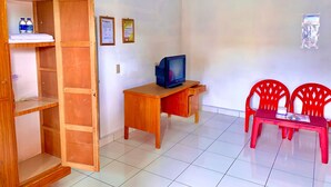 Una habitación con un escritorio de madera, televisión, una silla roja y una estantería con botellas.
